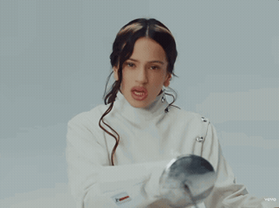 A Woman In A White Jacket Is Holding A Silver Ball In Her Hand GIF
