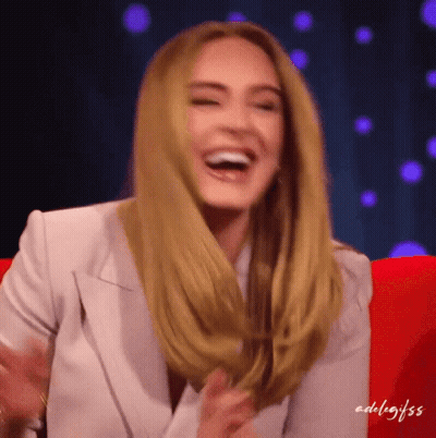 A Woman In A White Jacket Is Laughing While Sitting In A Chair GIF