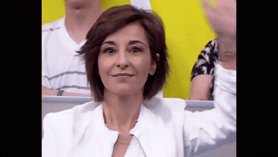 A Woman In A White Jacket Is Sitting In A Stadium With Her Arms Outstretched . GIF