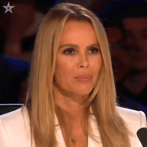 A Woman In A White Jacket Is Sitting In Front Of A Microphone And Making A Face . GIF