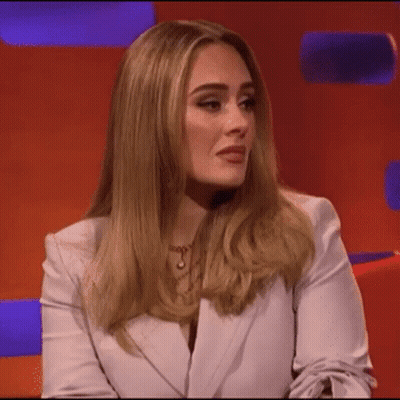 A Woman In A White Jacket Is Sitting On A Red Couch . GIF