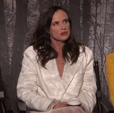 A Woman In A White Jacket Sits In A Chair With A Cup Of Coffee In Her Hand GIF