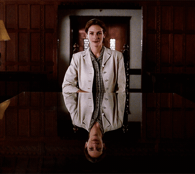 A Woman In A White Jacket Sits In A Chair With Her Head Down GIF