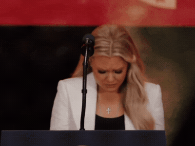 A Woman In A White Jacket Stands At A Podium With Her Eyes Closed GIF