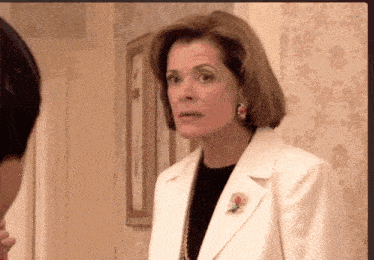 A Woman In A White Jacket With A Flower Pin On Her Jacket GIF