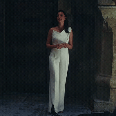 A Woman In A White Jumpsuit Is Standing In Front Of A Door GIF