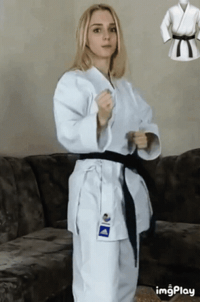 A Woman In A White Karate Uniform Is Standing Next To A Couch . GIF