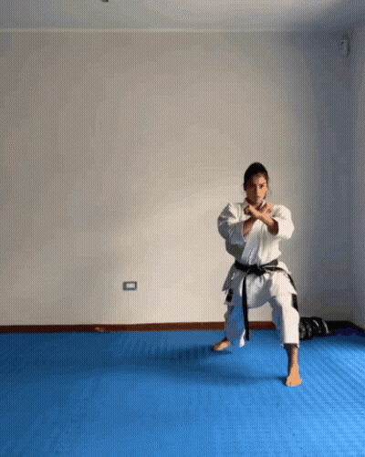 A Woman In A White Karate Uniform With A Black Belt Is Standing On A Blue Mat GIF