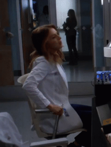 A Woman In A White Lab Coat Is Sitting In A Chair GIF