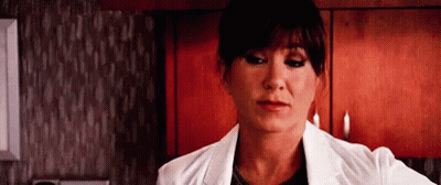 A Woman In A White Lab Coat Is Standing In A Kitchen Looking At The Camera . GIF
