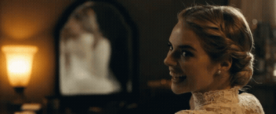 A Woman In A White Lace Dress Is Smiling In Front Of A Mirror GIF
