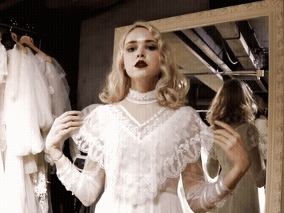 A Woman In A White Lace Dress Looks At Herself In A Mirror GIF