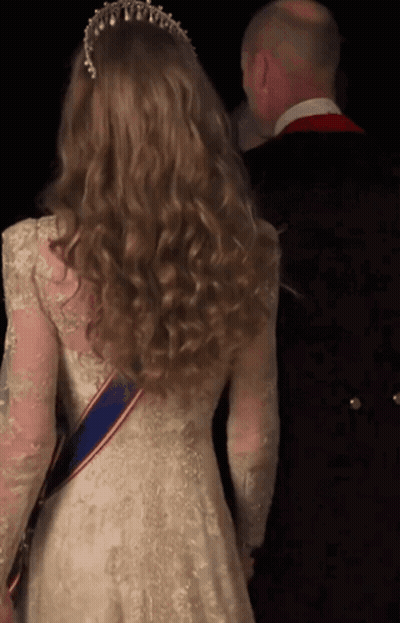 A Woman In A White Lace Dress With A Blue Sash Around Her Waist GIF