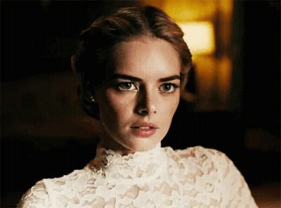A Woman In A White Lace Top Is Looking At The Camera With A Serious Look On Her Face . GIF