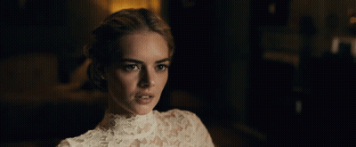 A Woman In A White Lace Top Looks At The Camera In A Dark Room GIF