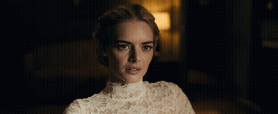 A Woman In A White Lace Top Looks At The Camera In A Dark Room GIF