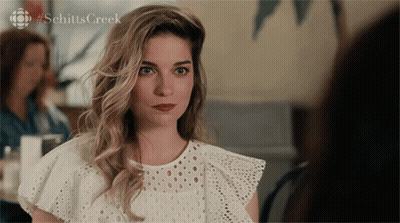 A Woman In A White Lace Top With #Schitts Creek On The Bottom GIF