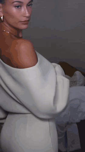 A Woman In A White Off The Shoulder Dress And Earrings GIF