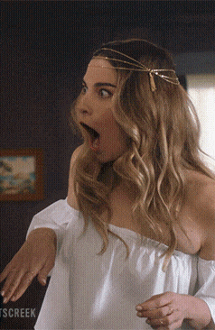 A Woman In A White Off The Shoulder Top Is Making A Surprised Face In Front Of A Sign That Says Tscreek GIF