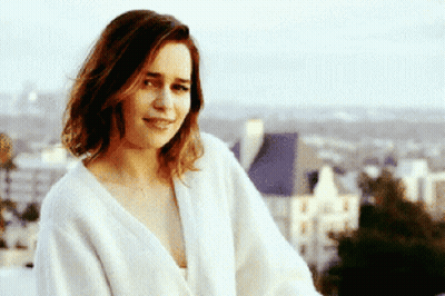 A Woman In A White Robe Is Smiling In Front Of A City GIF