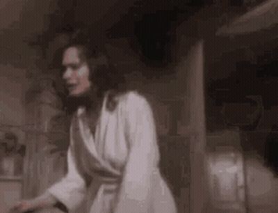 A Woman In A White Robe Is Standing In A Dark Room In A Bathroom . GIF