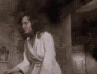 A Woman In A White Robe Is Standing In A Room . GIF