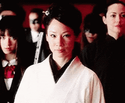 A Woman In A White Robe Is Standing In Front Of A Group Of People GIF