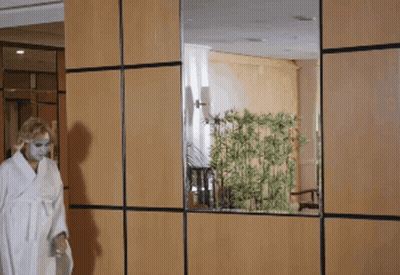 A Woman In A White Robe Is Standing In Front Of A Wooden Wall GIF