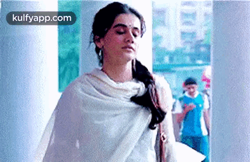 A Woman In A White Shawl Is Standing In A Hallway With Her Eyes Closed . GIF