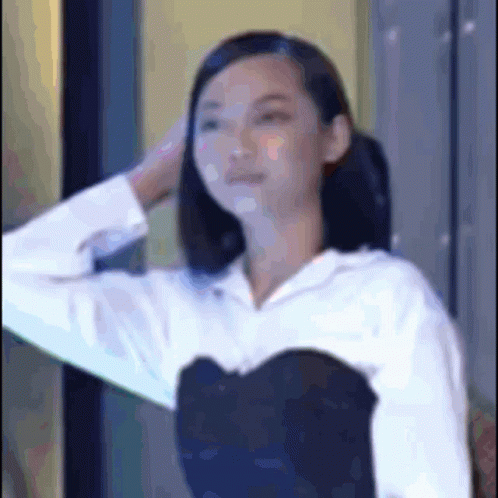 A Woman In A White Shirt And A Black Top Is Holding Her Hair . GIF