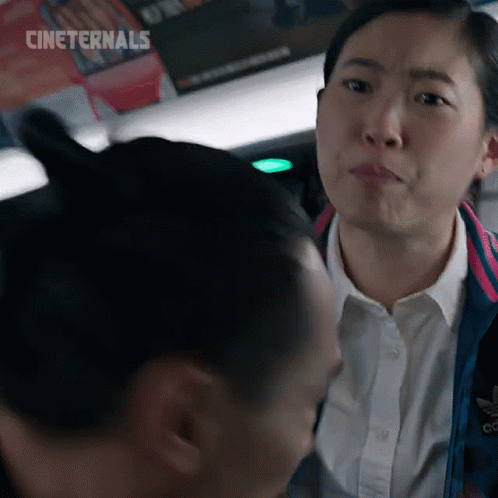 A Woman In A White Shirt And A Blue Jacket Is Looking At Another Woman . GIF