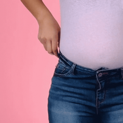 A Woman In A White Shirt And Blue Jeans Is Adjusting Her Waistband GIF