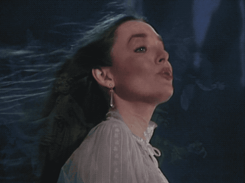 A Woman In A White Shirt And Earrings Looks Up GIF
