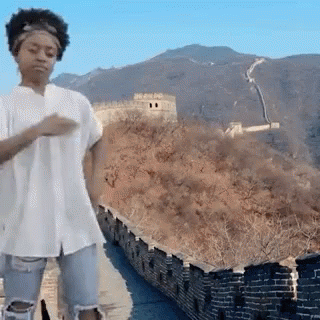 A Woman In A White Shirt And Ripped Jeans Is Dancing On The Great Wall Of China . GIF