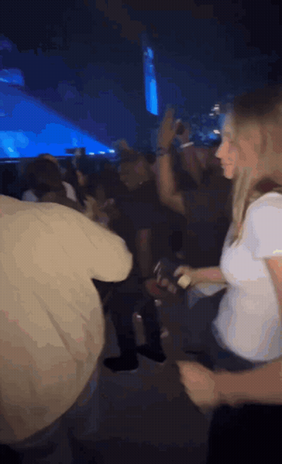A Woman In A White Shirt Is Dancing In A Crowd Of People At A Concert . GIF