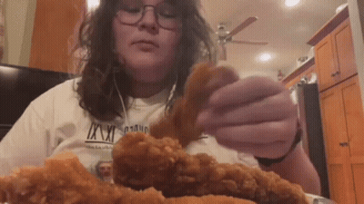 A Woman In A White Shirt Is Eating Fried Chicken . GIF