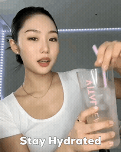 A Woman In A White Shirt Is Holding A Glass With A Pink Straw And The Words Stay Hydrated GIF