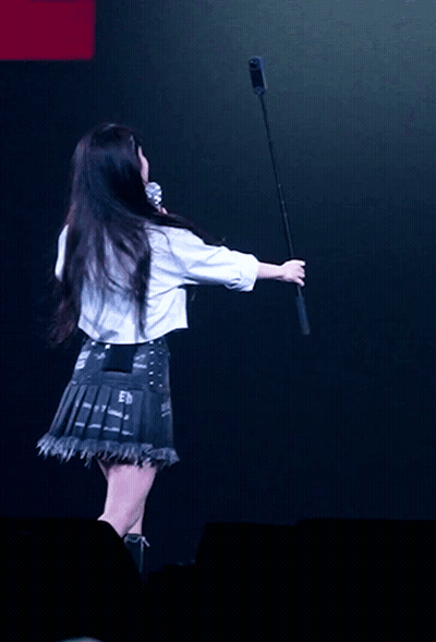 A Woman In A White Shirt Is Holding A Microphone In Her Hand GIF