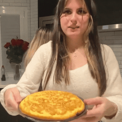A Woman In A White Shirt Is Holding A Pie GIF