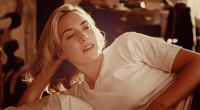A Woman In A White Shirt Is Laying Down With Her Head On Her Hand GIF