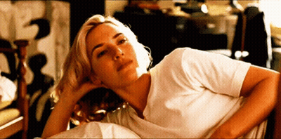 A Woman In A White Shirt Is Laying On A Bed With Her Head Resting On Her Hand GIF