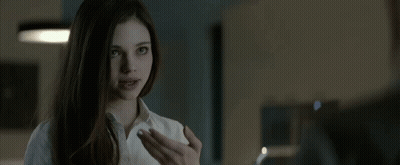 A Woman In A White Shirt Is Looking At A Man In A Dark Room . GIF