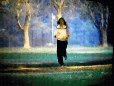 A Woman In A White Shirt Is Running In A Park With Trees In The Background .. GIF