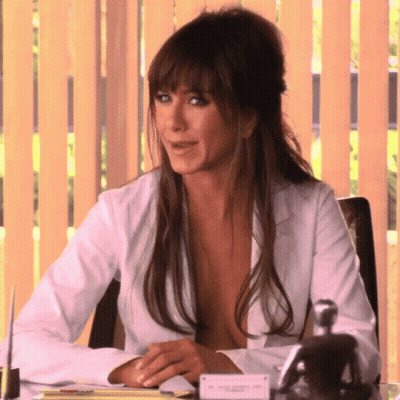 A Woman In A White Shirt Is Sitting At A Desk With A Name Tag That Says Jennifer Aniston GIF