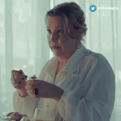 A Woman In A White Shirt Is Sitting At A Table With A Spoon In Her Hand And A Twitter Icon Above Her GIF