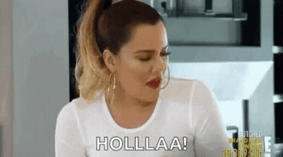A Woman In A White Shirt Is Sitting In A Kitchen Talking To Someone . GIF