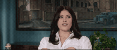 A Woman In A White Shirt Is Sitting In Front Of A Framed Picture GIF