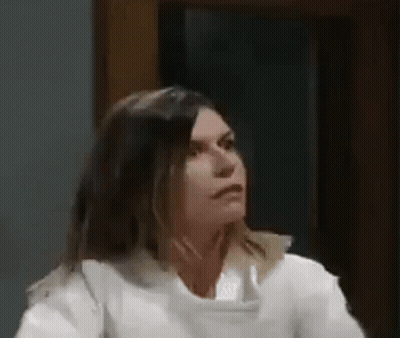 A Woman In A White Shirt Is Sitting In Front Of A Window And Looking At The Camera . GIF