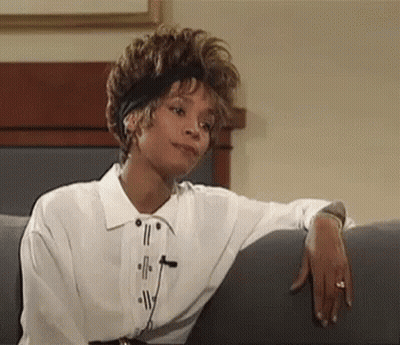 A Woman In A White Shirt Is Sitting On A Couch With Her Arm Resting On The Arm Of The Couch . GIF