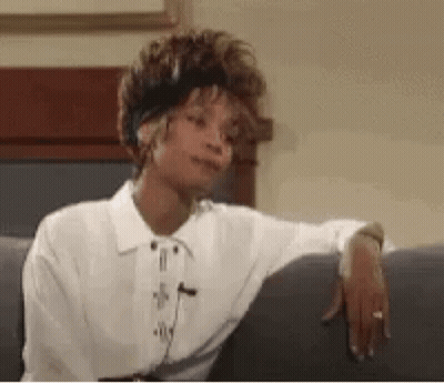 A Woman In A White Shirt Is Sitting On A Couch With Her Hand On Her Elbow . GIF